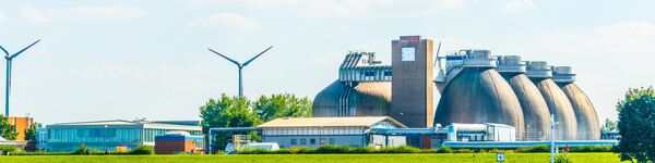 Image of an anaerobic digestion plant next to open water, with wind turbines in the background