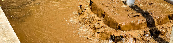 Sludge treatment in wastewater treatment. Brown liquid flowing in a concrete tank with pipes