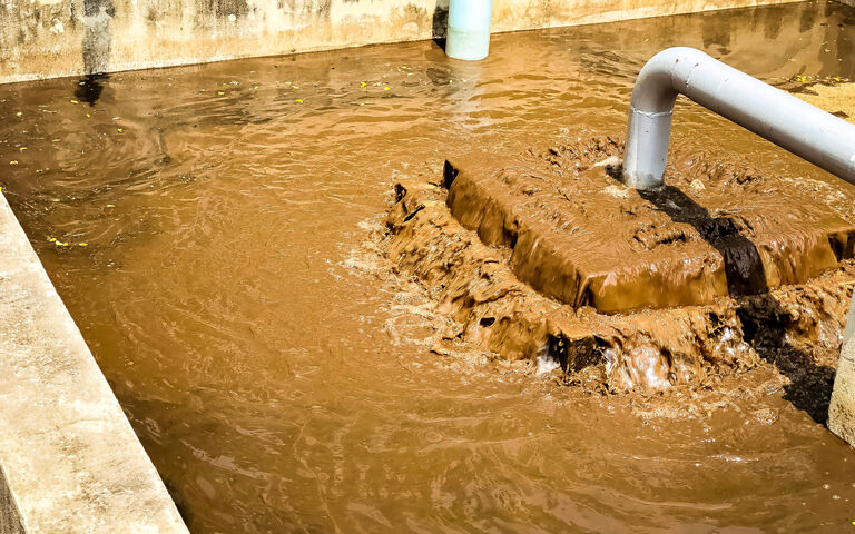 Sludge treatment in wastewater treatment. Brown liquid flowing in a concrete tank with pipes